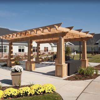 A wooden pergola in a landscaped garden area, surrounded by flowers and outdoor seating.