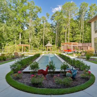 A beautifully landscaped garden with a central pool surrounded by colorful flowers and trees, creating a serene outdoor space.