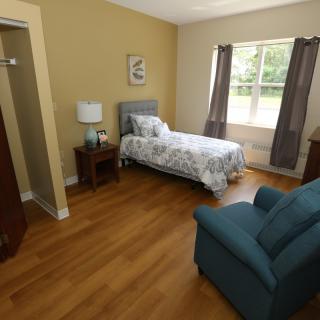 A cozy bedroom with a single bed, armchair, and wooden flooring.