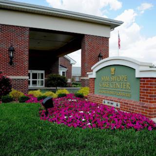 The welcoming entrance of a facility, featuring vibrant flowers and a prominent sign.