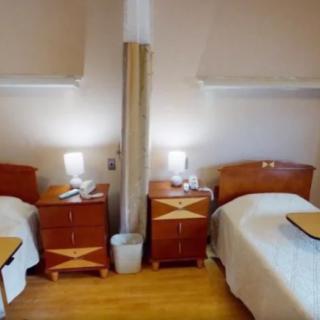 A hospital room featuring two beds separated by a curtain, each with a nightstand and lamp.