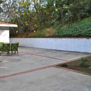 A spacious outdoor patio area with a table and chairs, bordered by greenery.