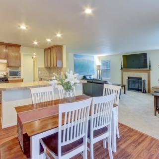 A spacious open-concept living space featuring a dining area with white chairs, a modern kitchen, and a cozy living room with a fireplace.