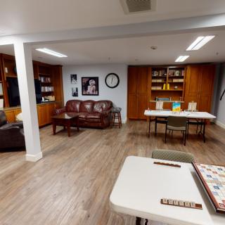 A cozy living room with wooden floors, a leather couch, bookshelves, and a game table featuring a Scrabble board.