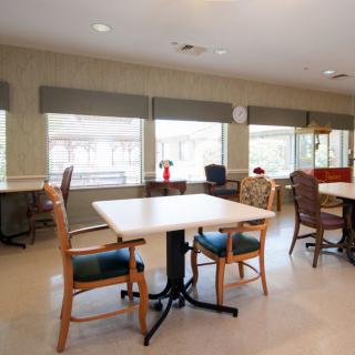 A brightly lit dining area with tables and chairs arranged near large windows.