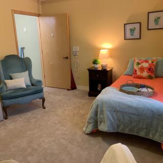 A cozy bedroom featuring a neatly made bed, an armchair, and a bedside lamp creating a warm ambiance.
