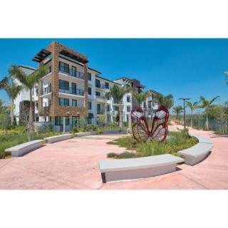 A modern apartment building with landscaped grounds and palm trees under a clear blue sky.