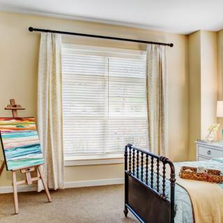 A cozy bedroom with an easel and art supplies next to a window with curtains.
