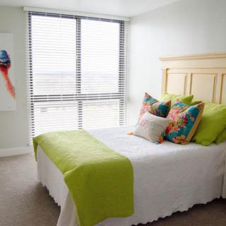 A modern bedroom with bright green accents and colorful pillows, featuring ample natural light from large windows.