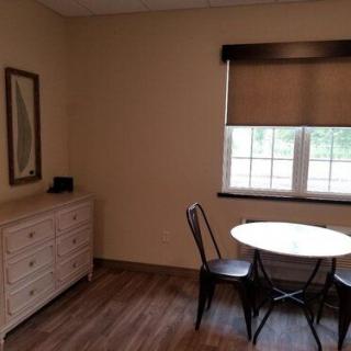 A simple room with a small round table, two chairs, a dresser, and a window with blinds.