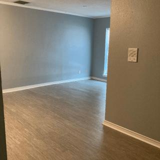 An empty room with grey walls and wood flooring, illuminated by natural light from a window.