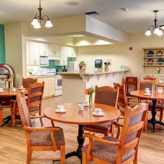 A cozy dining area with wooden tables and chairs, adjacent to a kitchen space.