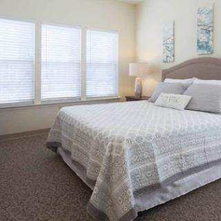 A serene and cozy bedroom featuring a neatly made bed, soft lighting, and ample natural light from the windows.