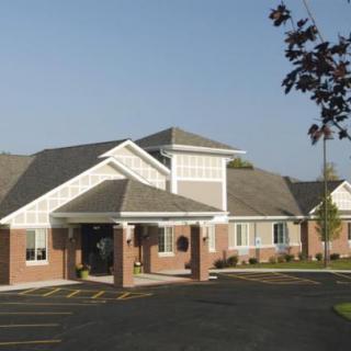 A brick building with a gabled roof and landscaped entrance under a clear sky.