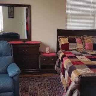 A cozy bedroom featuring a bed with a colorful patchwork quilt, a dresser with a mirror, and a comfortable chair.
