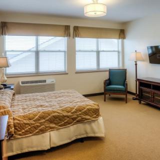 A neatly arranged hotel bedroom featuring a bed, windows, lamps, and a television.