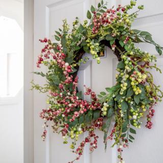 A decorative wreath with greenery and berries hanging on a door.