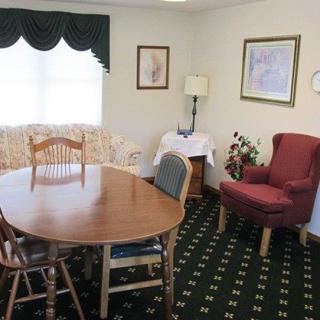 A cozy dining room with a wooden table, chairs, and an armchair, featuring artwork on the walls.