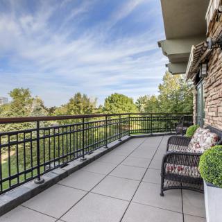 Spacious balcony with seating and a scenic view of trees under a clear sky.
