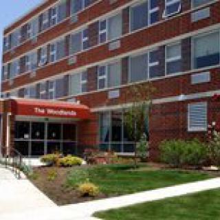 A red brick apartment building with a landscaped entrance and an awning.