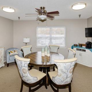A cozy dining room with a round table and patterned chairs, complete with a ceiling fan and window view.