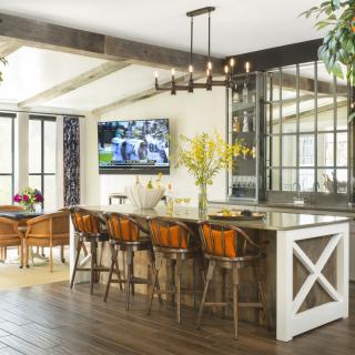 A modern kitchen and dining area featuring a row of bar stools, a TV on the wall, and stylish interior decor.