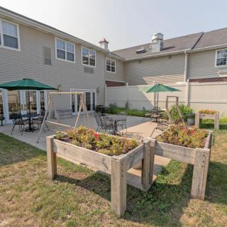An outdoor patio area featuring tables, chairs with umbrellas, planters, and a two-story building in the background.