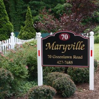 A sign for Maryville located at 70 Greenlawn Road, surrounded by landscaping and a white fence.