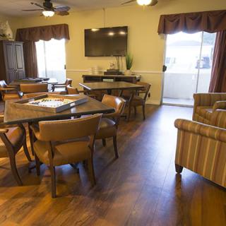 A cozy living room with wooden flooring, featuring a television, tables, and chairs.