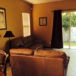 A cozy living room with a sofa and a lamp beside a window, featuring a sliding glass door leading outside.