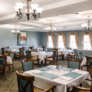 An elegant dining room with neatly arranged tables, white tablecloths, and chandeliers.
