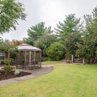 A peaceful garden scene featuring a gazebo, a manicured lawn, and lush trees.