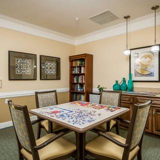 A cozy dining room with a table set for a puzzle, surrounded by chairs and decorated with artwork and vases.
