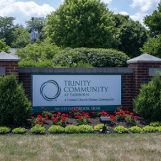 Entrance sign to Trinity Community surrounded by greenery and flowers.