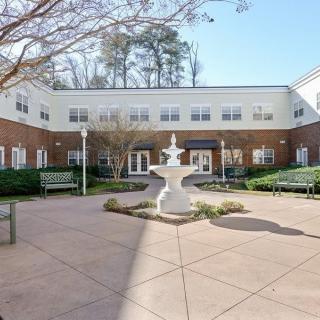 A courtyard featuring a central fountain surrounded by benches in front of a two-story building.