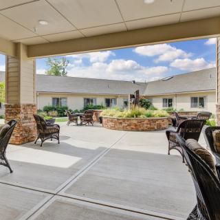 A view of an outdoor patio area with seating, situated in a landscaped courtyard beside a building on a cloudy day.