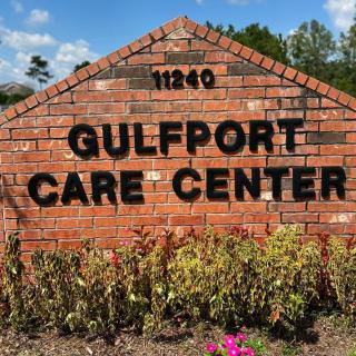 A brick sign for Gulfport Care Center with landscaping in front and a partly cloudy sky in the background.