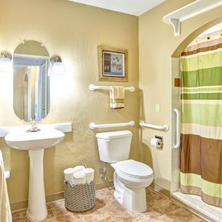 A well-lit bathroom with a pedestal sink, toilet, and a shower with a colorful curtain.