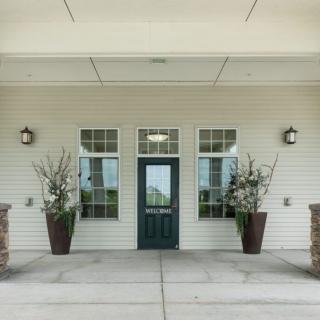 A building entrance with a dark door, flanked by windows and potted plants.