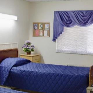 A tidy hospital room with a single bed covered in blue bedding, decorated with flowers and curtains.