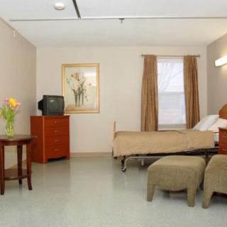 A simple hospital room with a single bed, dresser, television, and table with flowers.
