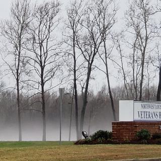 A foggy winter scene featuring bare trees and a welcoming sign.