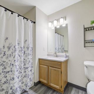 A modern bathroom features a wooden vanity with a sink and mirror, alongside a shower curtain and toilet.