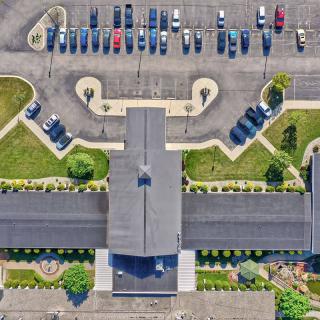 Aerial view of a building with a parking lot and landscaped surroundings.