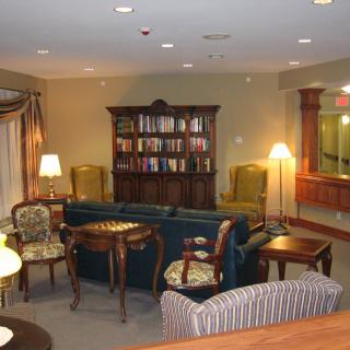 A cozy indoor reading area with a bookshelf, chairs, and lamps.