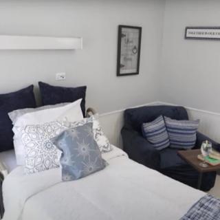 A cozy bedroom with a neatly made bed featuring multiple pillows, a comfortable chair, and simple, modern decor.