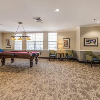 A spacious billiards room with a pool table, seating, and artwork on the walls.