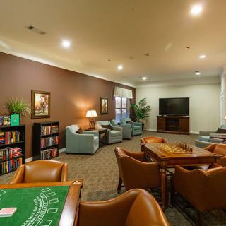 A cozy lounge area featuring armchairs, wooden tables, a television, and bookshelves.