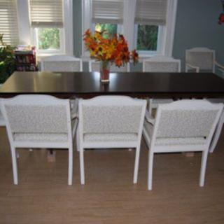 A dining room with a dark wooden table, several white chairs, and a vase of flowers.