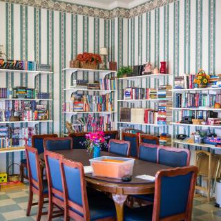 A cozy library room with a round table and chairs surrounded by colorful bookshelves.